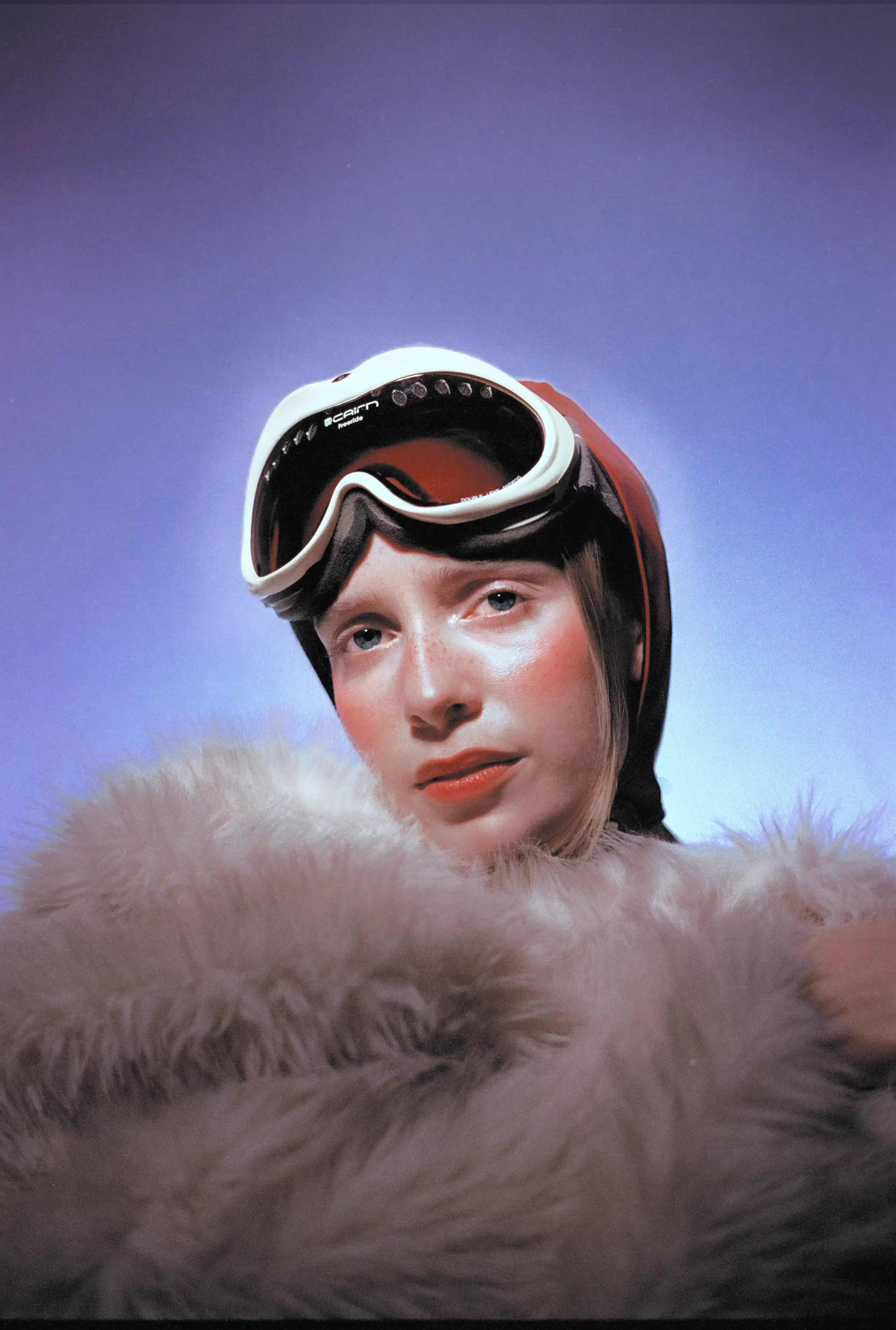 Portrait of Marine D. with goggles pushed up on her forehead above a pale fur collar, violet gradient behind