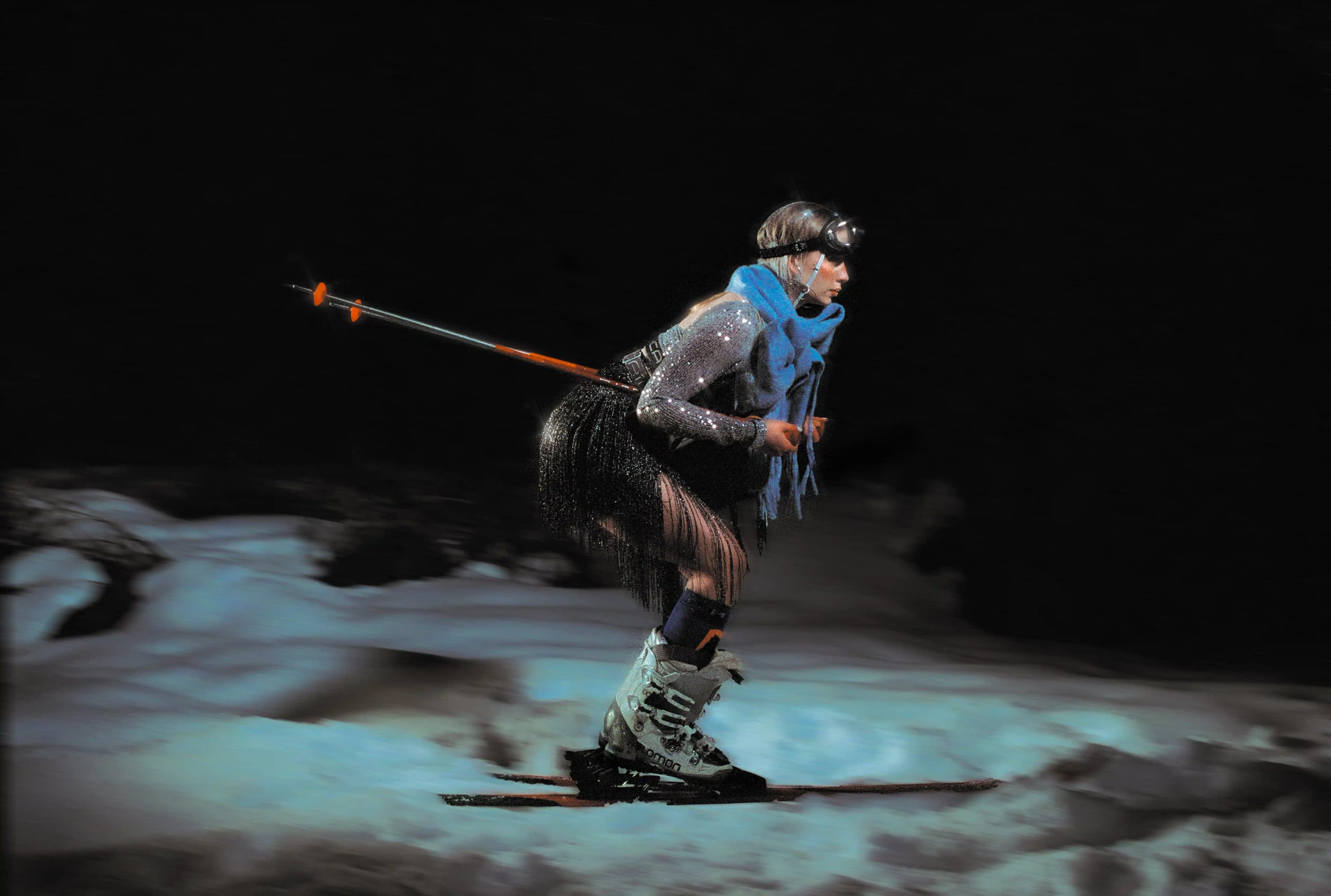 Blurred night frame of Marine D. skiing across a lit patch of snow, poles trailing behind her