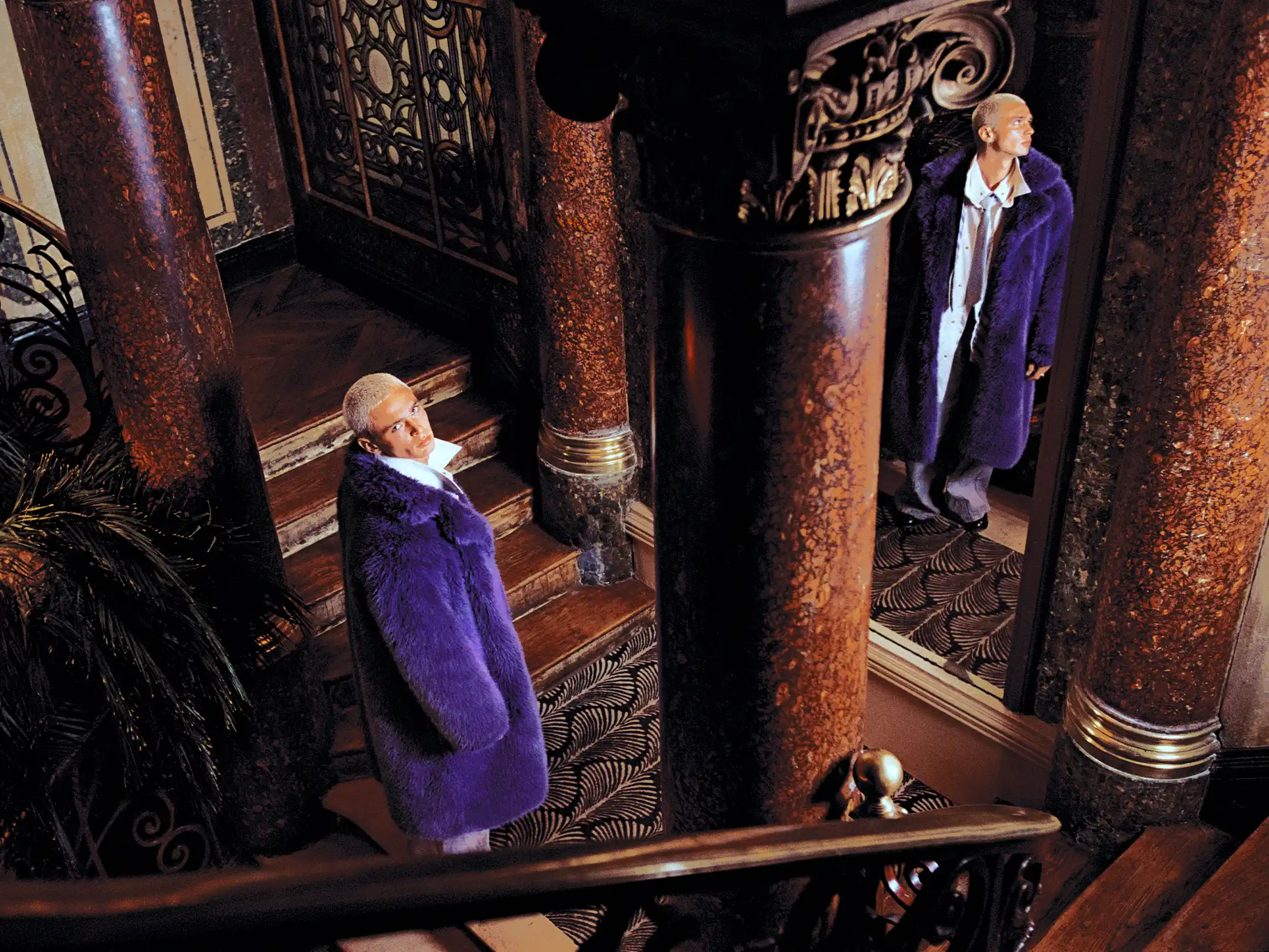 High-angle frame of Matheo in a purple fur coat on a marble staircase, a second version of him standing in the doorway beyond