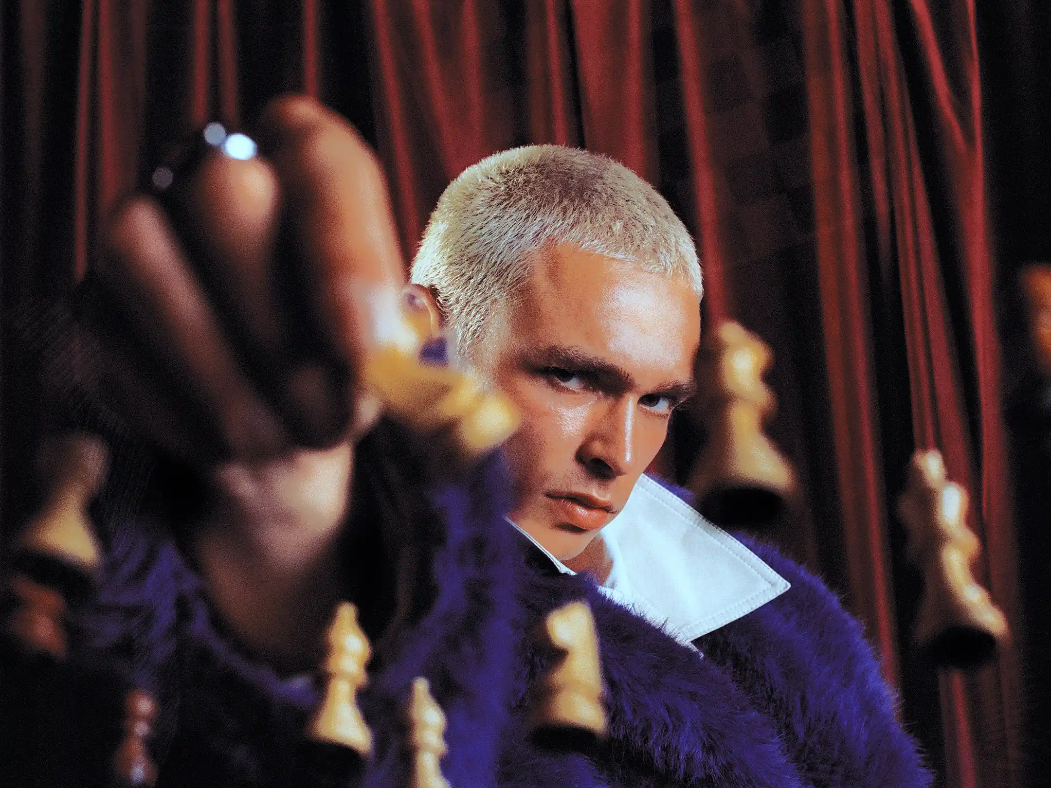 Tight portrait of Matheo shot through out-of-focus chess pieces against a red velvet curtain