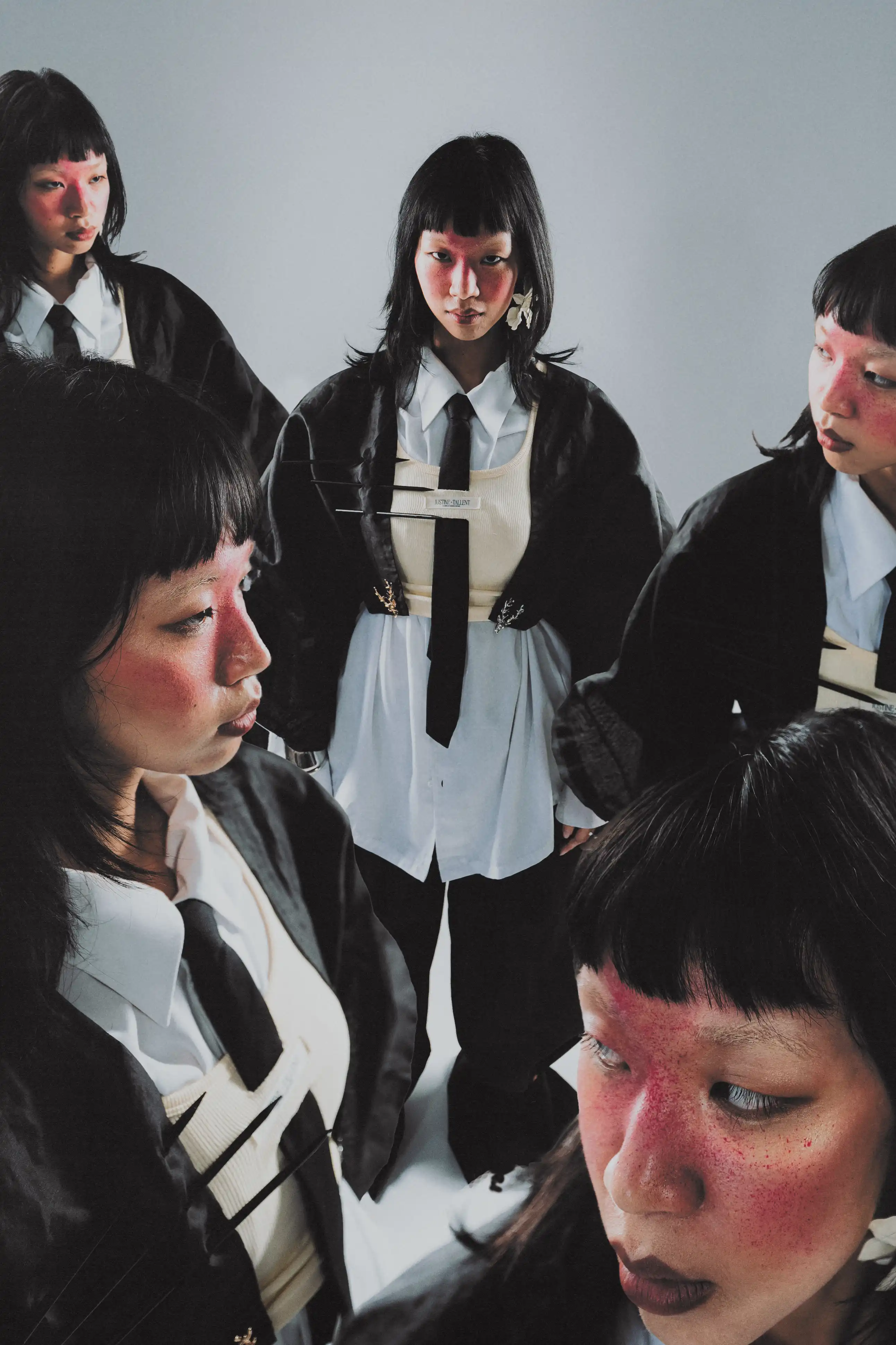 Five copies of Karine P. in blazer, shirt and tie circling the camera and looking down into the lens