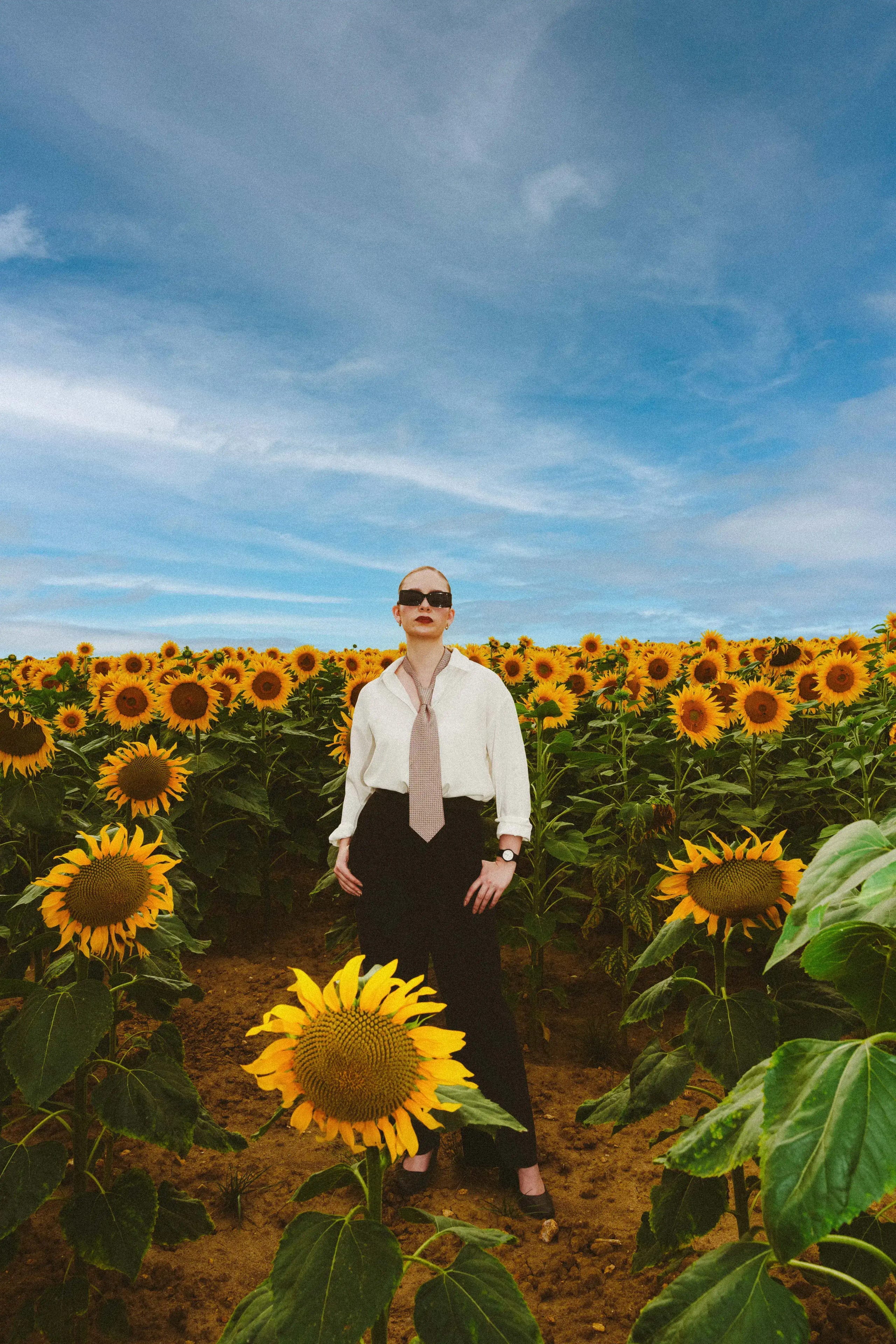 Full-length frame of Marine D. standing still among the sunflowers under a wide summer sky