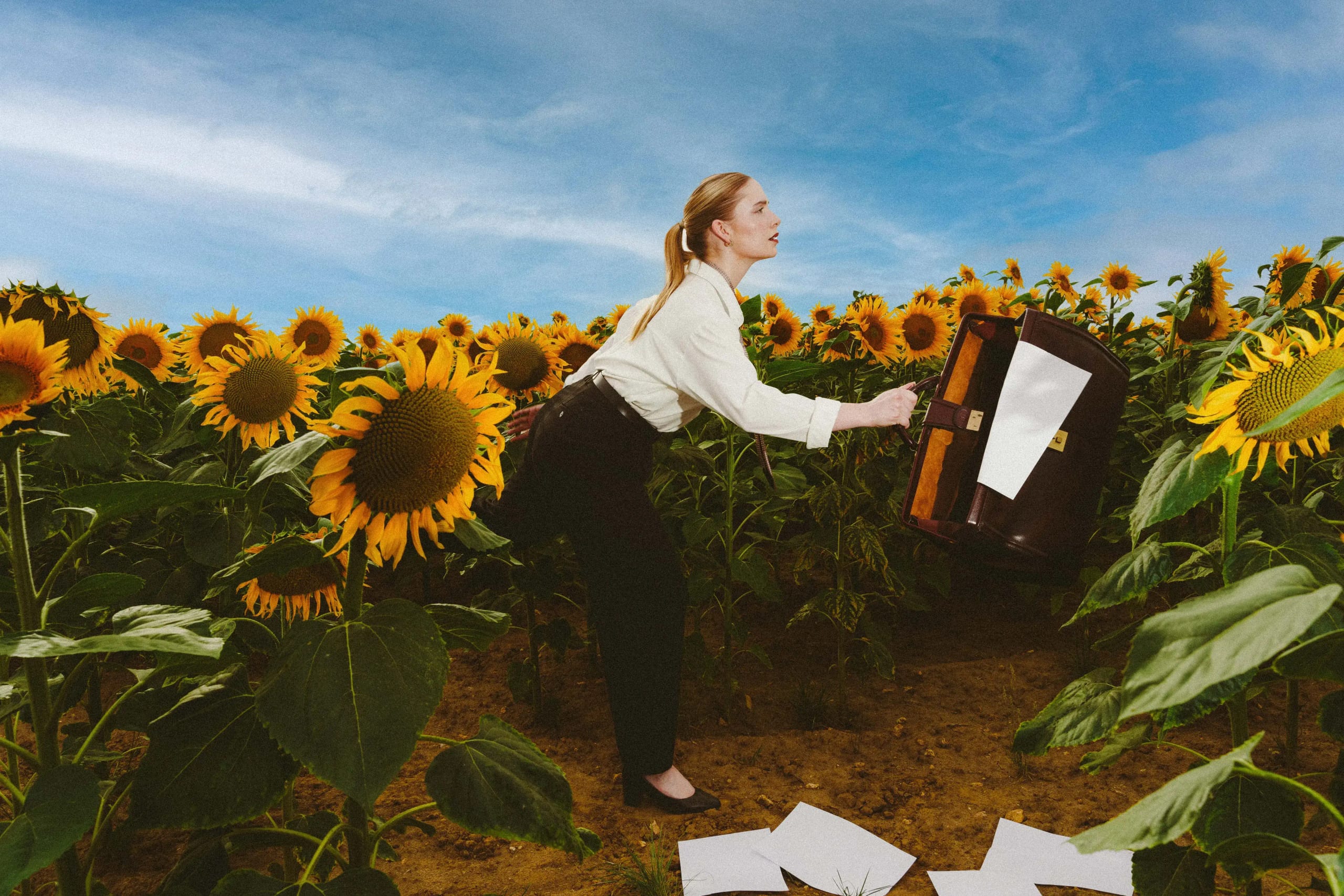 Marine D. throwing the open bag forward, loose sheets of paper scattered across the soil between the stems
