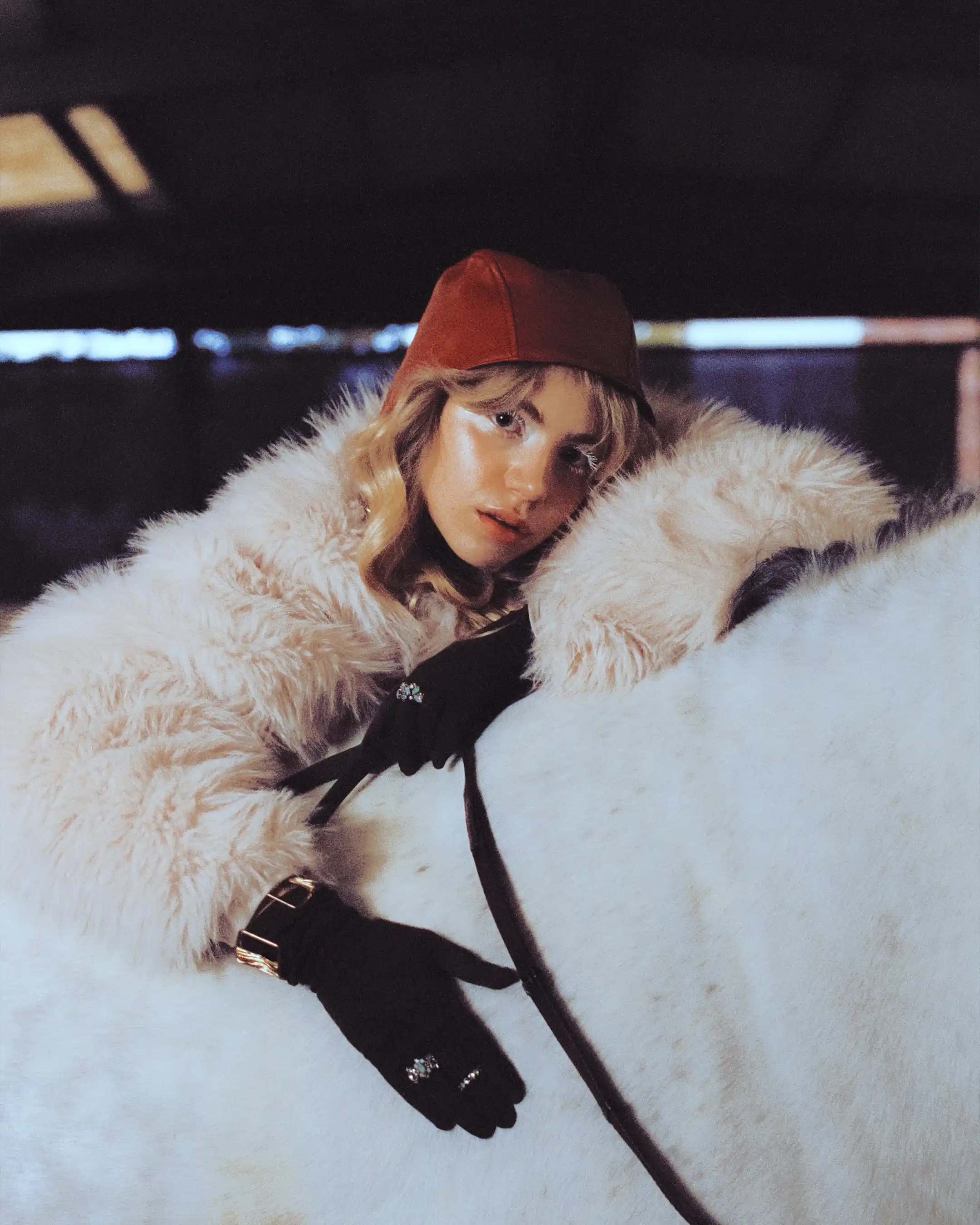 Romane Parc leaning over Cassalo's white back in a shearling coat and red cap, arena lights blurred behind