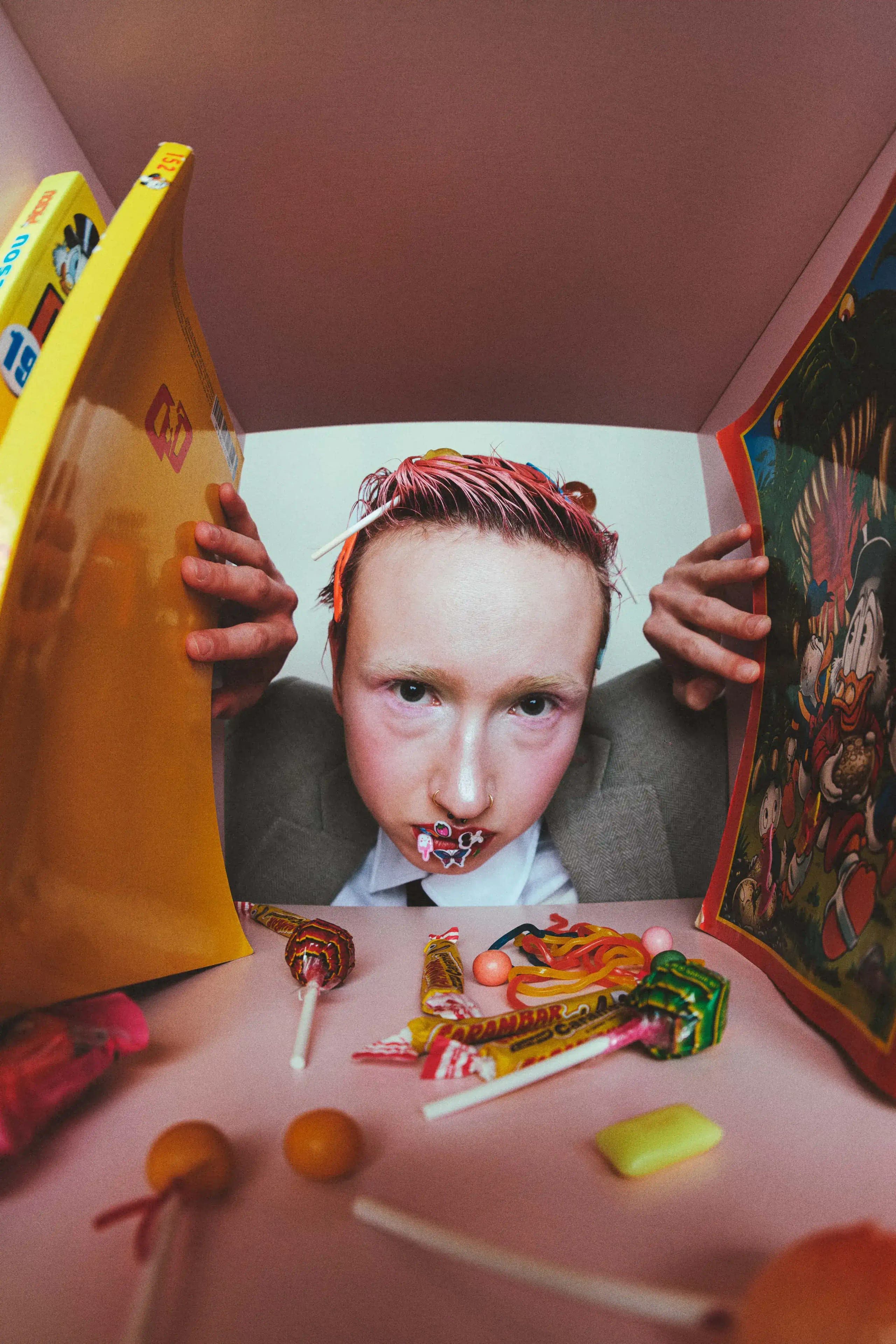 Model peering over a table of sweets and lollipops between two open picture books, pink set and school tie