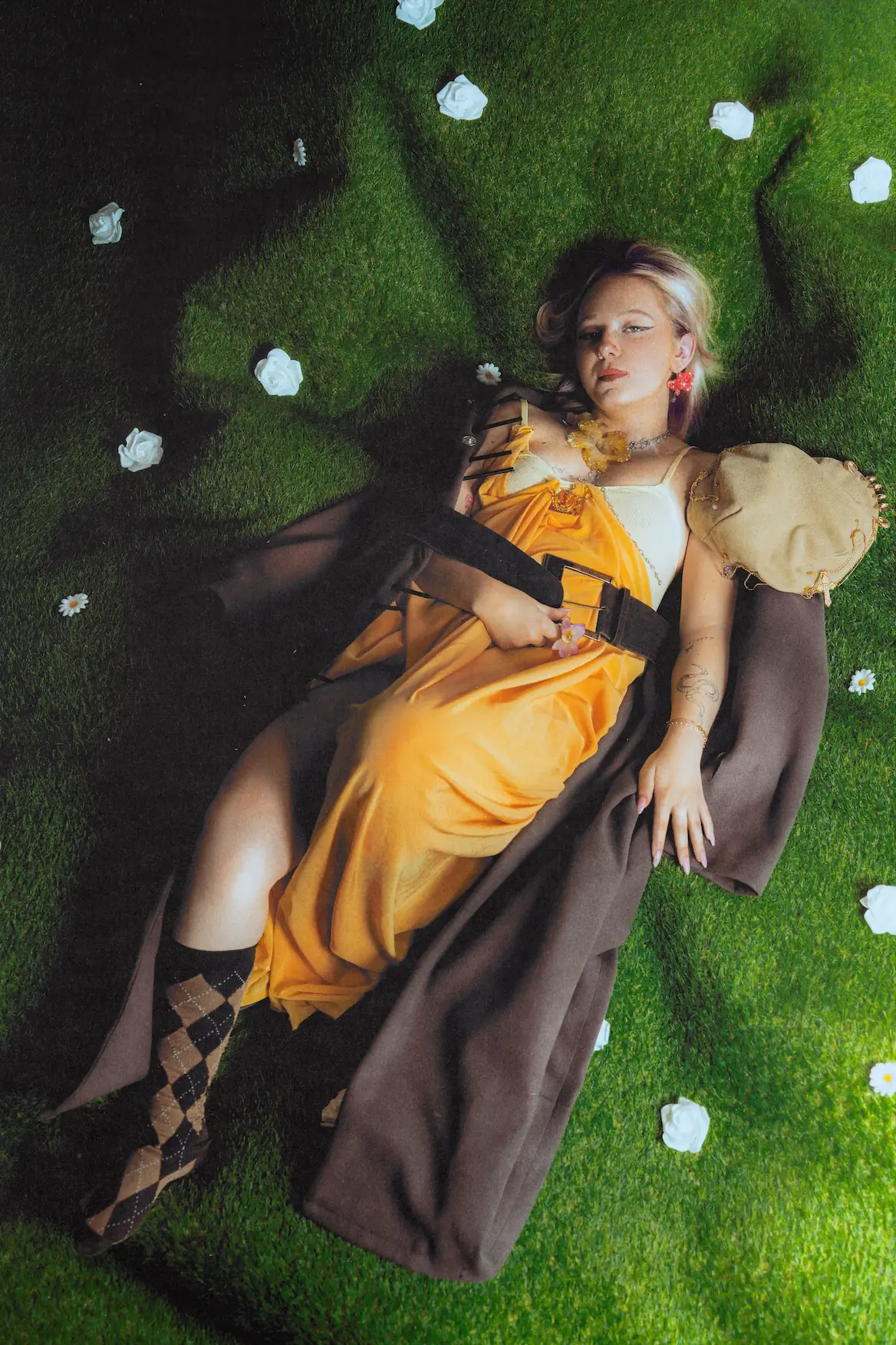 Overhead frame of Julie lying on the grass set in a yellow satin dress and oversized brown tailoring