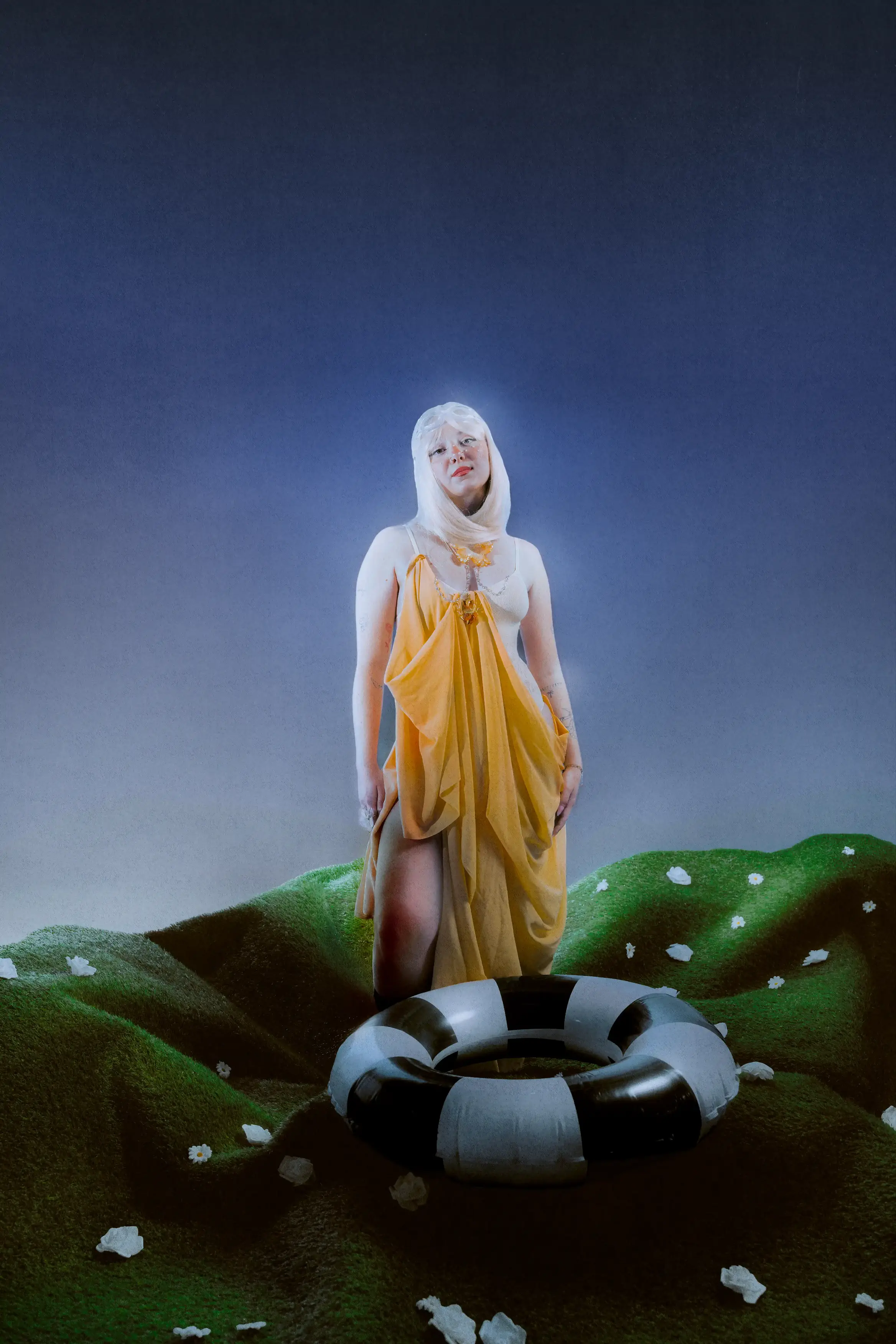 Julie standing on a mound of artificial grass in a draped yellow gown and white wig, a life ring at her feet