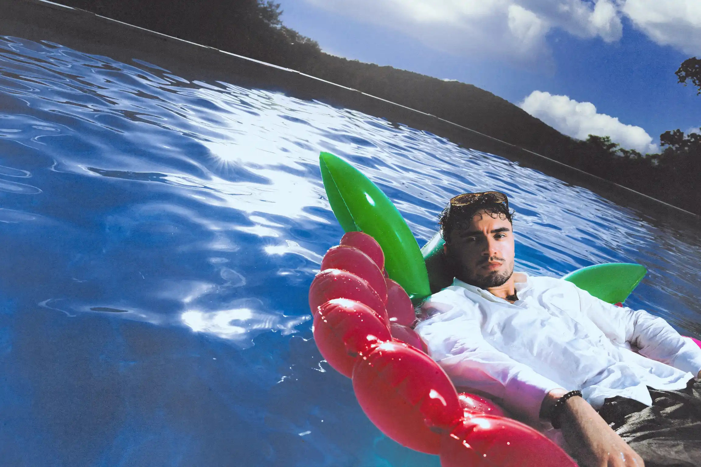 Tilted horizon as Tyron B. reclines on a cherry-shaped inflatable, sunlight scattering across the water