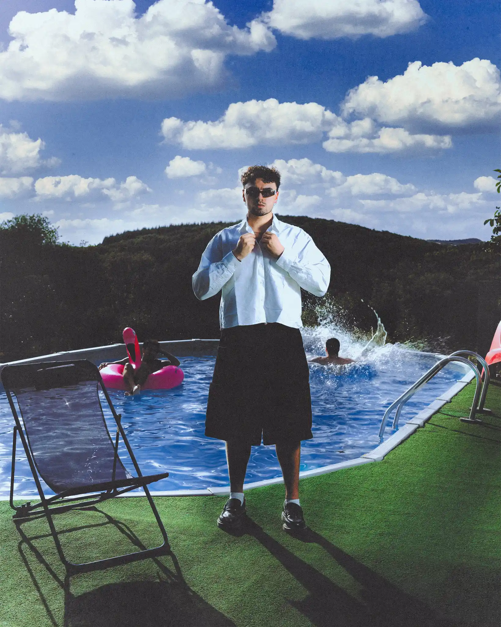 Tyron B. in sunglasses adjusting his shirt collar at the edge of an above-ground pool, friends splashing behind him