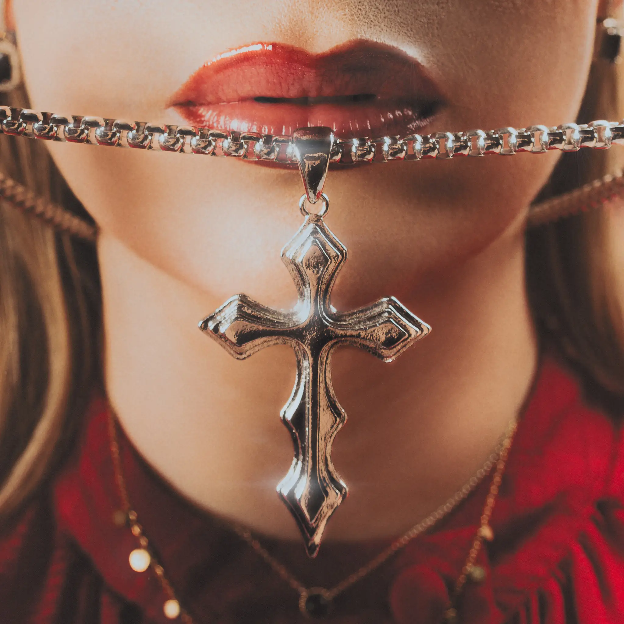 Close crop on Marine D. holding a chain-hung silver cross between glossed lips, red lace top