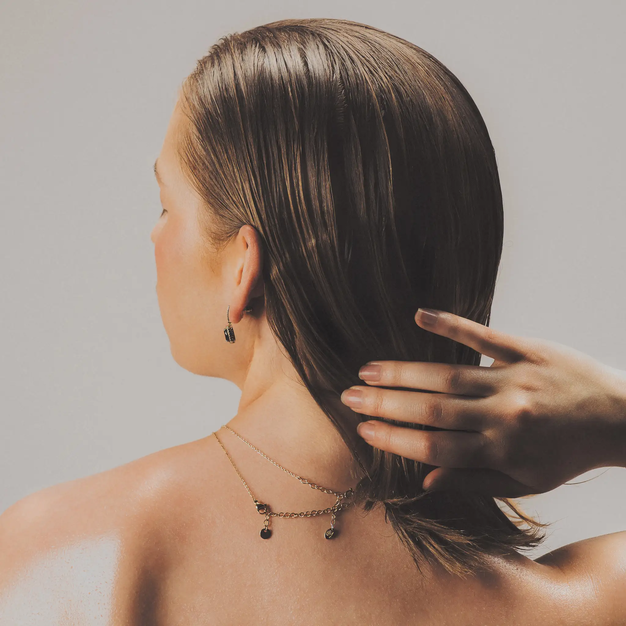 Marine D. photographed from behind, one hand sweeping slicked hair off a bare shoulder