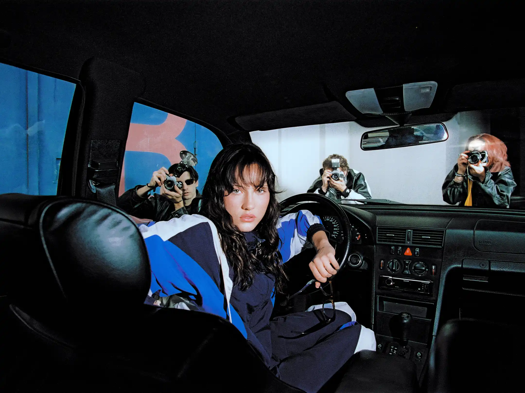 Taabzzi at the wheel of a car as photographers press their lenses against the windows