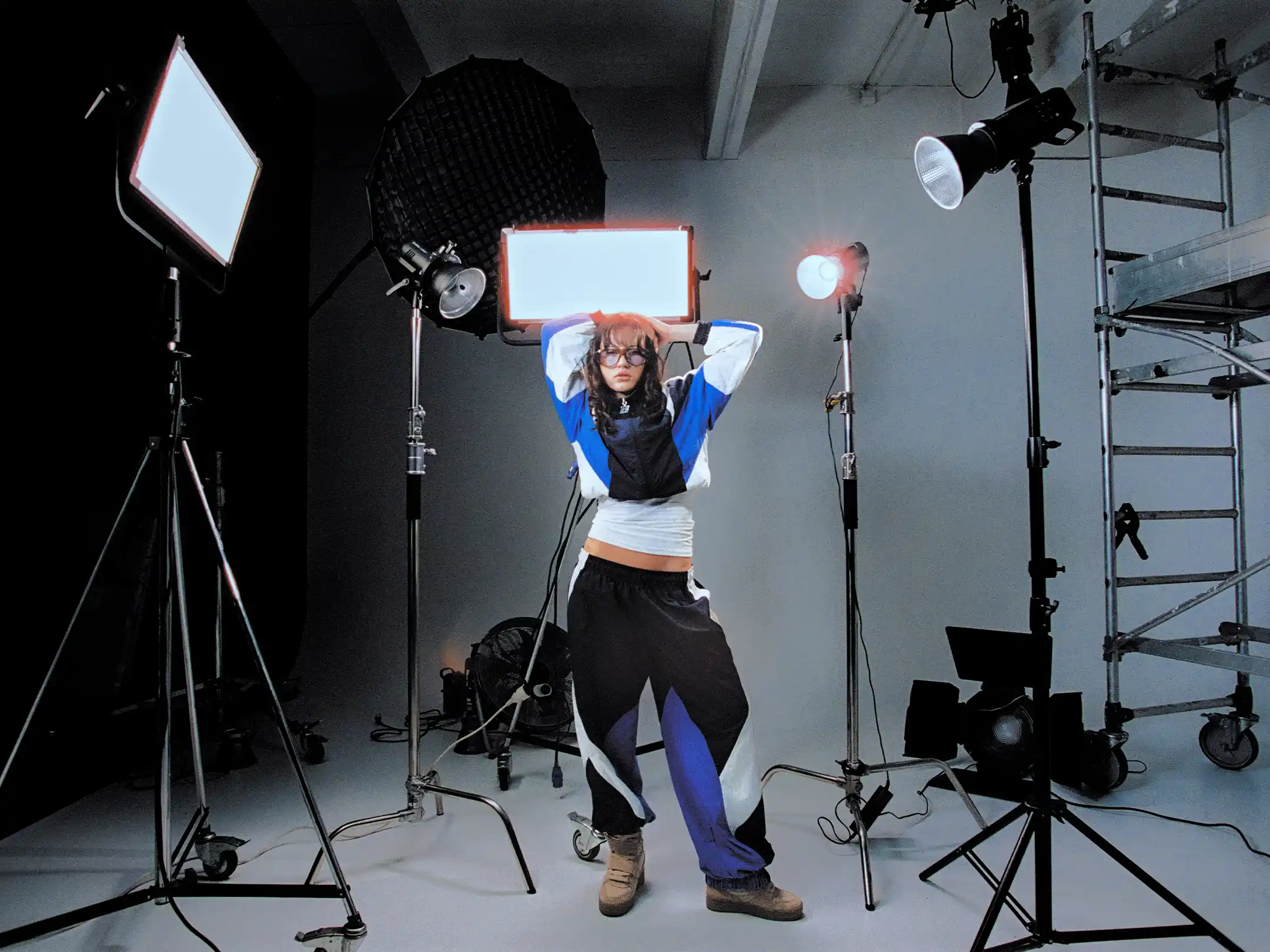 Taabzzi posing with both arms raised in the middle of a ring of studio lights and stands