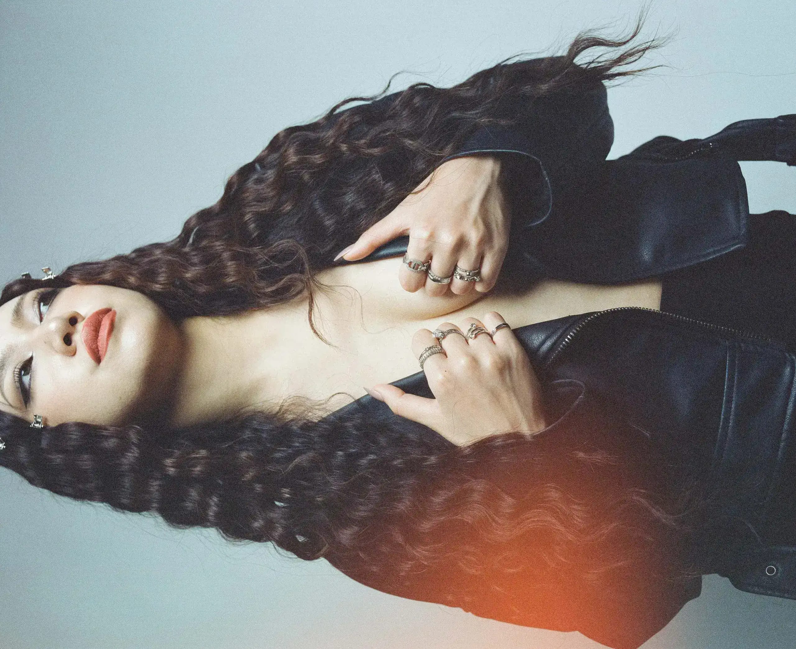 Miho S. against a pale backdrop, crimped hair and black leather jacket pulled off the shoulder, warm light leak across the frame