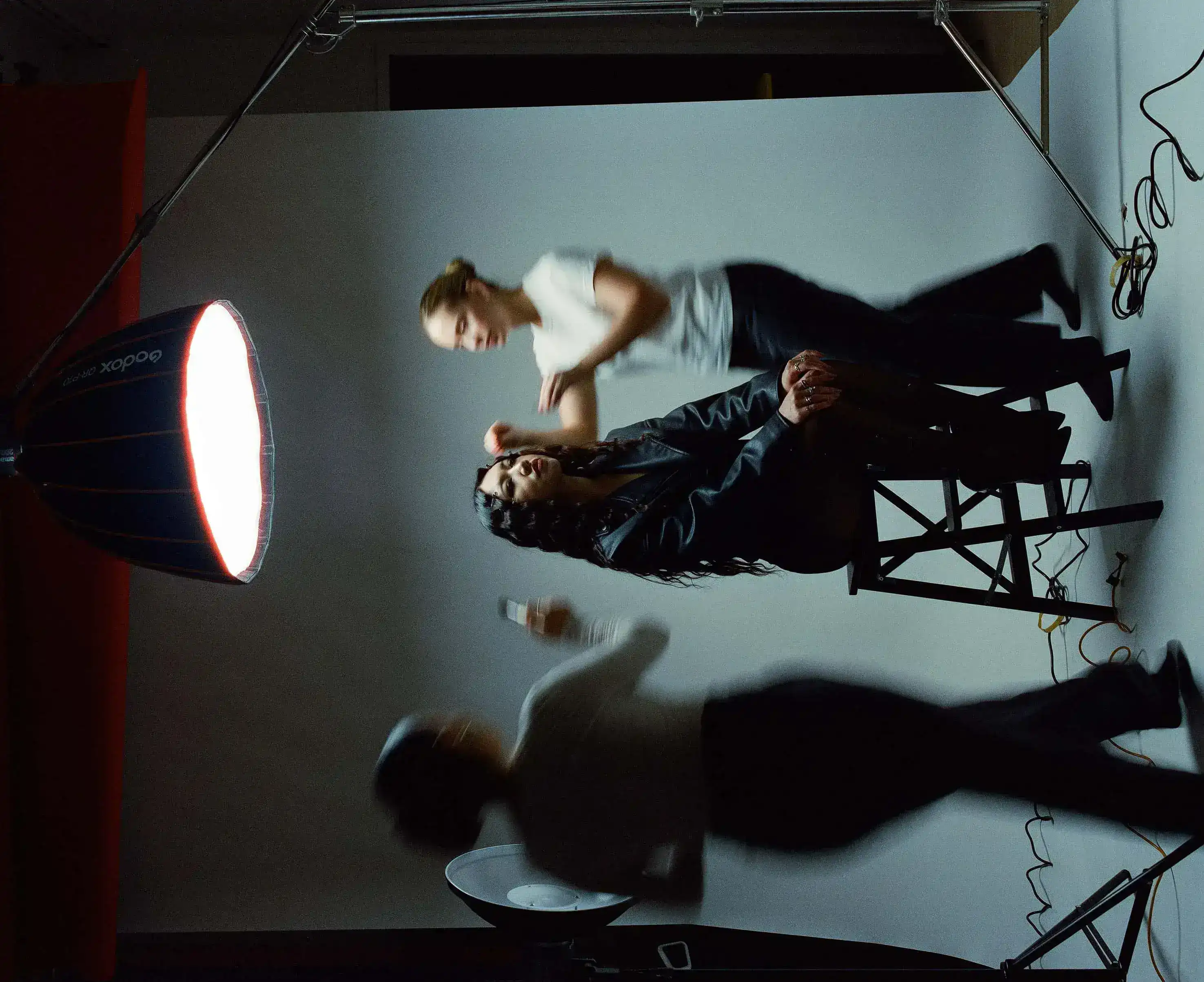 Wide frame of the studio set — softbox, stands and cables while the crew moves around the model between takes
